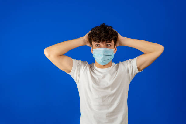 istock Amazed worried young man 20s in basic white shirt sterile face mask safe from coronavirus virus covid-19 during quarantine put hands on head isolated on blue background 1337880830