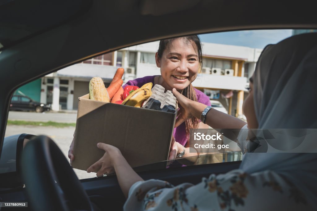 Volunteers hands out food at drive through food bank A female volunteer hand out free food to car driver during a drive through food bank charity campaign in early morning. Charity and Relief Work Stock Photo