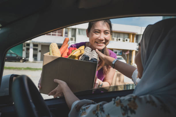 Volunteers hands out food at drive through food bank A female volunteer hand out free food to car driver during a drive through food bank charity campaign in early morning. altruism photos stock pictures, royalty-free photos & images