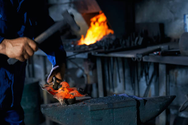 istock Man in overalls forging molten metal on anvil 1337883230