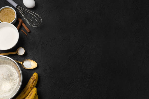 Bulk ingredients for banana bread in bowls and bananas on black background