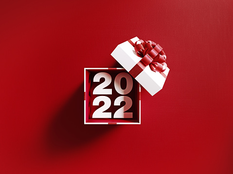 2022 is coming out of a white gift box tied with red ribbon on red background. Horizontal composition with copy space. Directly above. Great use for Christmas related gift concepts.