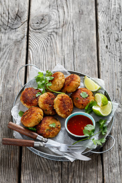 tod man pla, torte di pesce tailandesi con lime, coriandolo e salsa di peperoncino dolce su un piatto nero su un tavolo rustico di legno, vista verticale dall'alto - fish cakes immagine foto e immagini stock