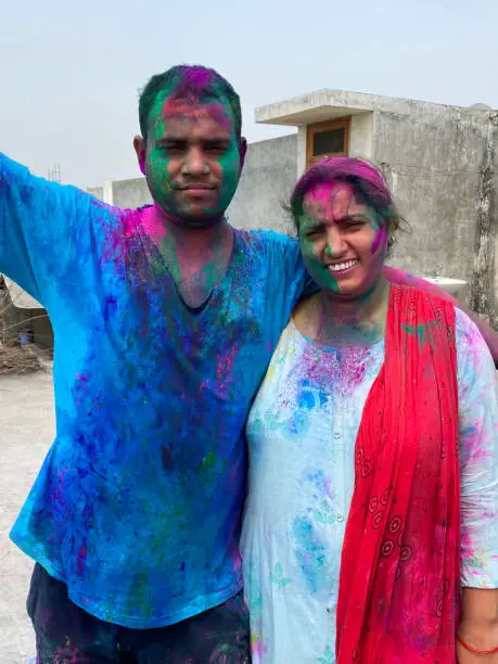 Photo of Image of Hindu Indian man and woman wearing Kurta and Salwar Kameez traditional clothing, covered in paint powder colour gulal rang, messing around at Holi festival of colours and love paint fight, smiling looking at camera