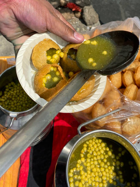 Close-up image of Indian street food, panipuri being served with flavoured water (mint / masala) and chickpeas in a single use bowl, snacks at family Holi celebration stock photo