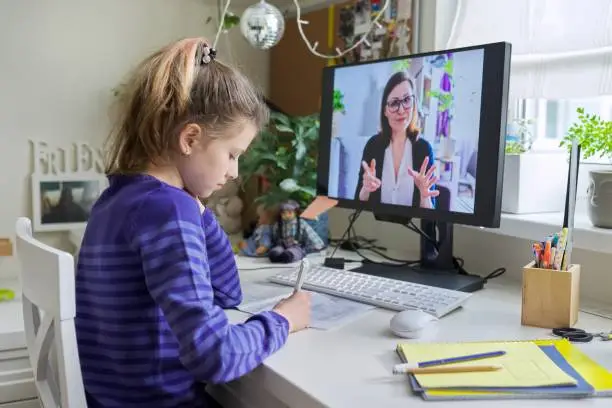 Young child girl studying with teacher remotely on computer using video call, an individual online lesson, videoconference application. Education, technology, children, pre-teens, e-learning concept