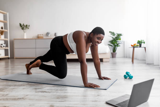 istock Plus size Afro woman having strength workout, following web tutorial on laptop, running with hands on floor at home 1337890495