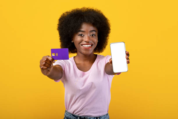 istock Mobile application for shopping. Happy black lady showing empty smartphone screen and credit card over yellow background 1337891552