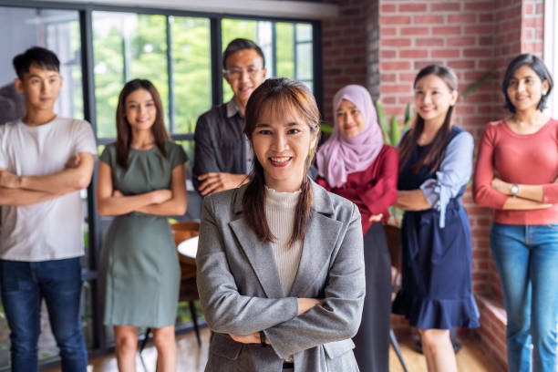 Portrait of young businesswoman standing in an office with her colleagues in the background stock photo