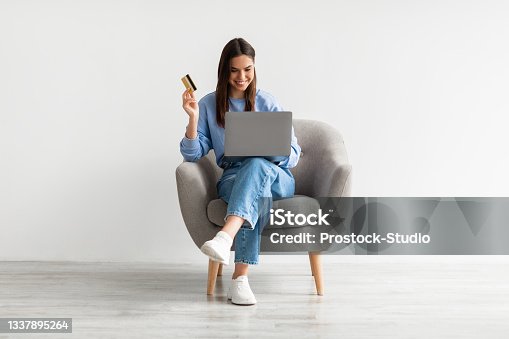 istock Online shopping, e-commerce, remote banking. Young woman sitting in armchair with laptop and credit card, buying on web 1337895264