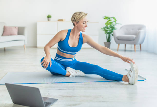 istock Happy Woman In Sportswear Stretching Leg On Mat Using Computer 1337895416