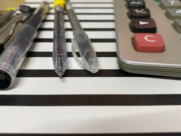 Pens and calculator on black and white stripe clipboard