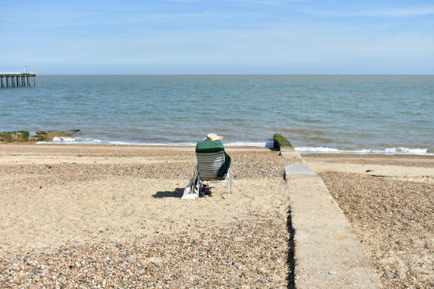 Whitstable, UK - Sep 6th 2020  A senior lady sits on a bench looking out to sea in Tankerton, Whtistable. She has a dog with her. There is a row of beach huts in front of her
