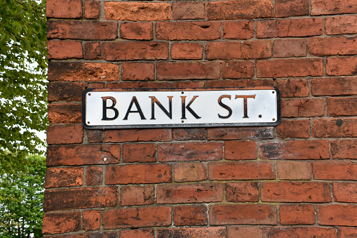 close up of unusual old metal street sign, text reading BANK STREET,  situated outside on a building exteriors red brick wall