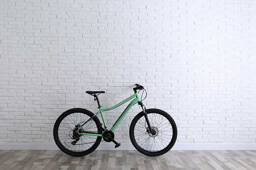 Modern green bicycle near white brick wall. Space for text