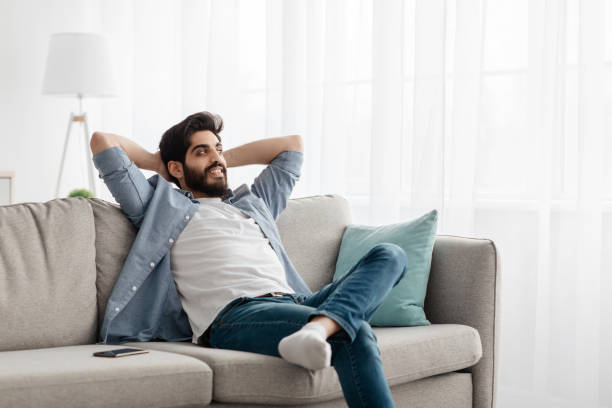 istock Home comfort. Young arab man relaxing on cozy sofa, leaning back on couch with hands behind head, free space 1337905421