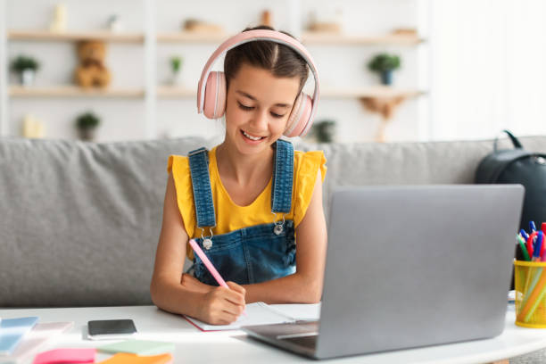 istock Smiling girl sitting at desk, using laptop, writing in copybook 1337906387