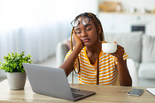 exhausted black woman sitting in front of laptop, drinking coffee - ressaca imagens e fotografias de stock