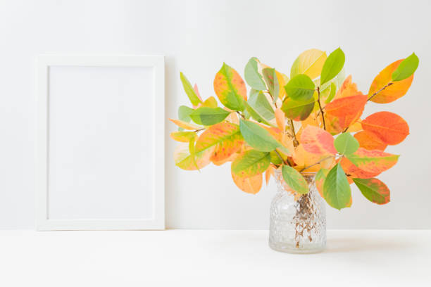 istock Home interior with decor elements. Mockup with a white frame, colorful autumn leaves in a vase on a light background 1337907329