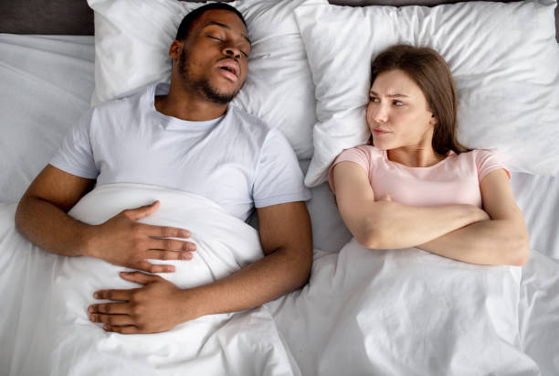 dresinsicht einer irritierten jungen frau, die sich über ihr schwarzen mann ärgert, der im bett schnarcht - couple love snoring sleeping stock-fotos und bilder