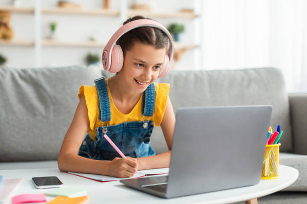istock Smiling girl sitting at desk, using laptop, writing in textbook 1337912534