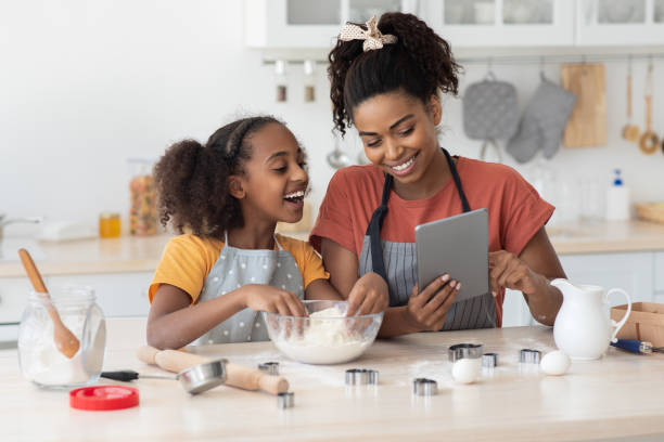 Black mummy and daughter cooking at home, using tablet