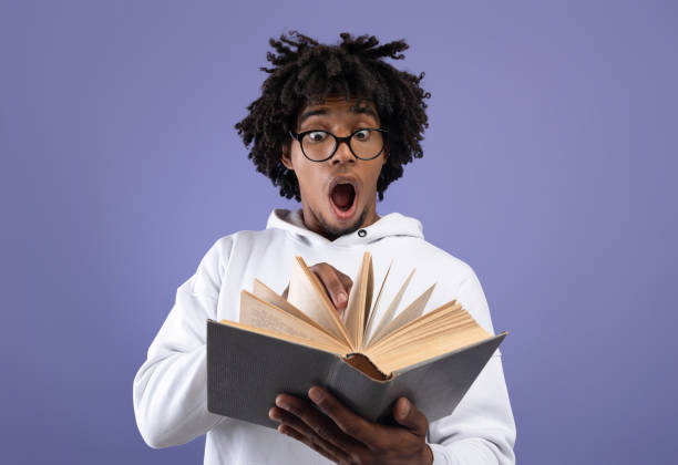 Black teen student looking at textbook in shock, afraid of too much homework on violet studio background Black teen student looking at textbook in shock, afraid of too much homework on violet studio background. Emotional African American teenager studying for difficult college exam, reading book nerd teenager stock pictures, royalty-free photos & images