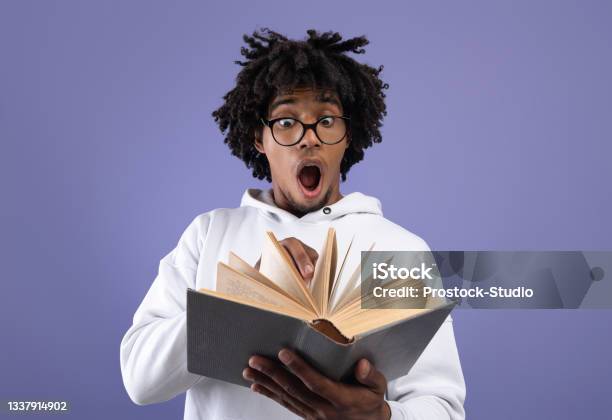 Black Teen Student Looking At Textbook In Shock Afraid Of Too Much Homework On Violet Studio Background Stock Photo - Download Image Now