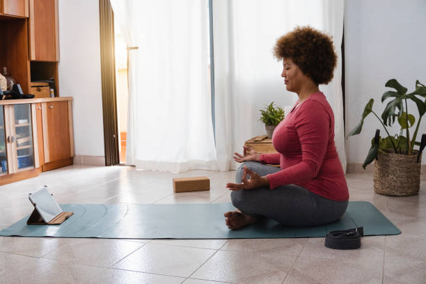 african senior woman doing yoga remote class meditation at home - sport and healthy lifestyle concept - focus on tablet - women yoga yoga class mature adult imagens e fotografias de stock