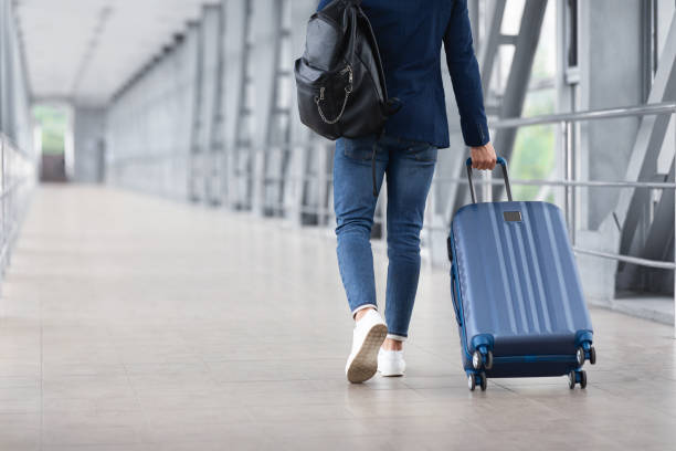 vista trasera de un hombre irreconocible que camina con una maleta en la terminal del aeropuerto - mochila bolsa fotografías e imágenes de stock