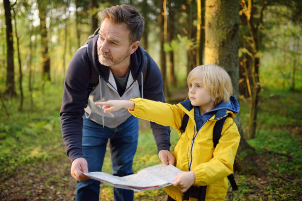 학생과 그의 성숙한 아버지는 함께 하이킹과 자연을 탐험. 숲에서 오리엔티어링 하는 동안 지도를 찾고 아빠와 어린 소년. 아이들을위한 모험, 스카우트 및 하이킹 관광. - orienteering 뉴스 사진 이미지