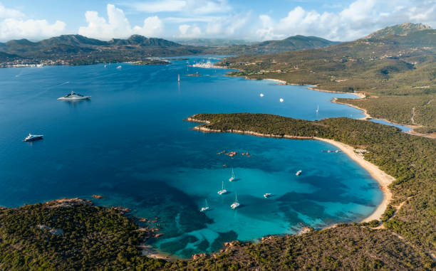 View from above, stunning aerial view of a green coastline with a white sand beach and and boats sailing on a turquoise water at sunset. Cala di volpe beach, Costa Smeralda, Sardinia, Italy. stock photo