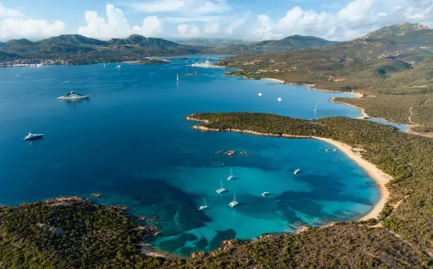 View from above, stunning aerial view of a green coastline with a white sand beach and and boats sailing on a turquoise water at sunset. Cala di volpe beach, Sardinia, Sardinia, Italy.