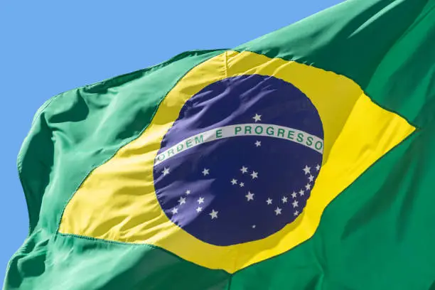 detail of Brazil flag fluttering in the blue sky. Translation: order and progress.