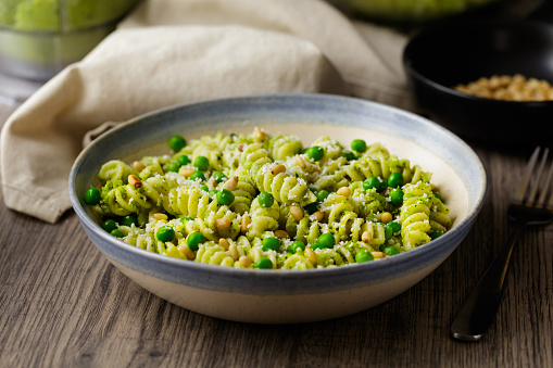 Healthy fusilli pasta with green peas bowl service with vegan broccoli pesto sauce, roasted pine nuts and shaved hard coconut cream