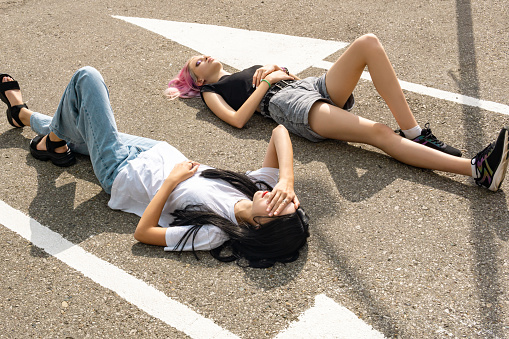 two teenager girls have fun lying on an empty road parallel to the markings