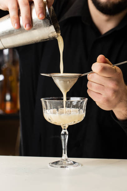 istock Professional bartender pours orange alcoholic cocktail from shaker into glass using sieve. Blurred view 1337935627