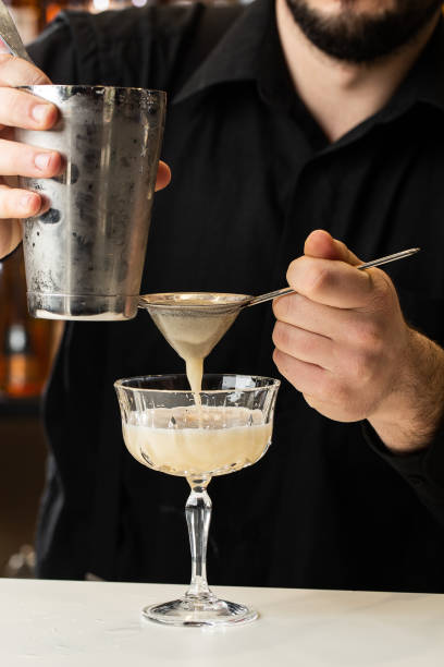 istock Professional bartender pours orange alcoholic cocktail from shaker into glass using sieve. Blurred view 1337935630
