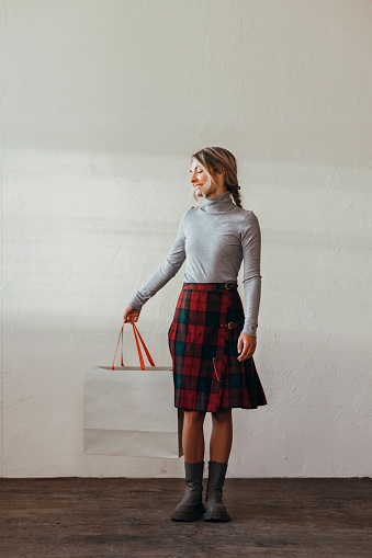 Smiling female holding shopping bag and looking away while standing over a white wall