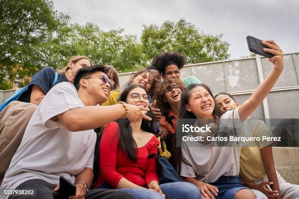 Group Of Multiethnic Students Taking Selfies With Mobile Phone Teenagers Using A Smart Phone And Having Fun Together Stock Photo - Download Image Now