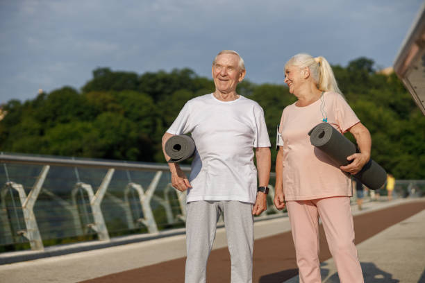 istock Cheerful mature couple with rolled mats ready for workout on footbridge 1337938367