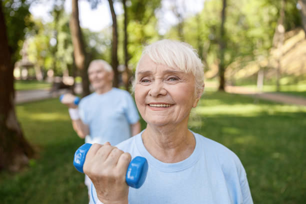 istock Cheerful senior lady does exercises with dumbbell training with partner in park 1337938491