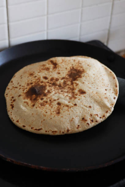 Image of inflated roti / chapatti cooking in kitchen non-stick frying pan, wholewheat atta flour, elevated view, focus on foreground stock photo