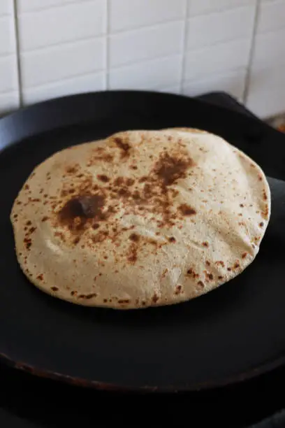 Stock photo showing a roti (also known as chapati) made from wholewheat atta flour being cooked in a non-stick frying pan. A roti is a traditional Indian flatbread often eaten with curries.
