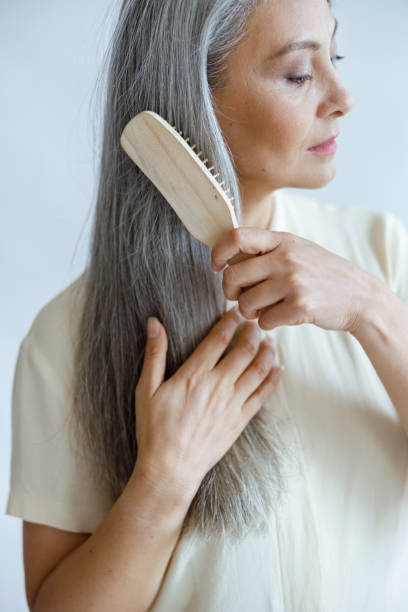 istock Tranquil middle aged Asian model brushes long hoary hair posing on light background 1337942915