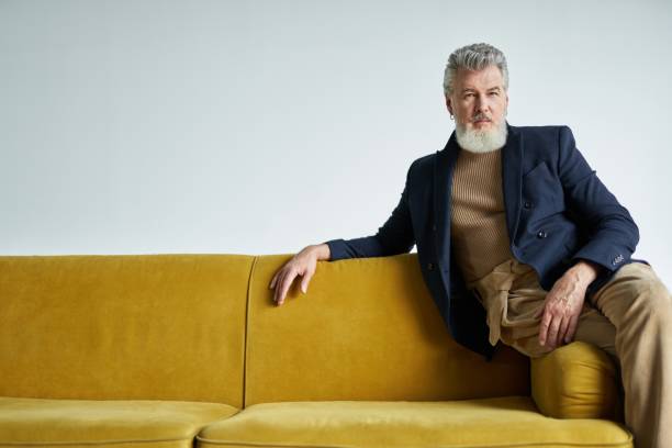 istock Stylish middle aged business man with a beard looking at camera while posing, sitting on yellow sofa indoors 1337943289