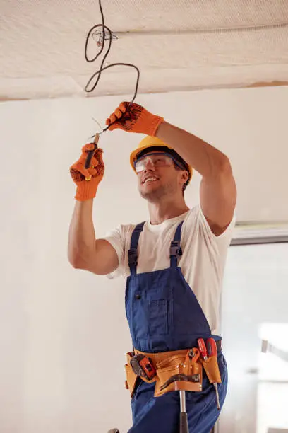 Photo of Cheerful electrician repairing electric cable on ceiling