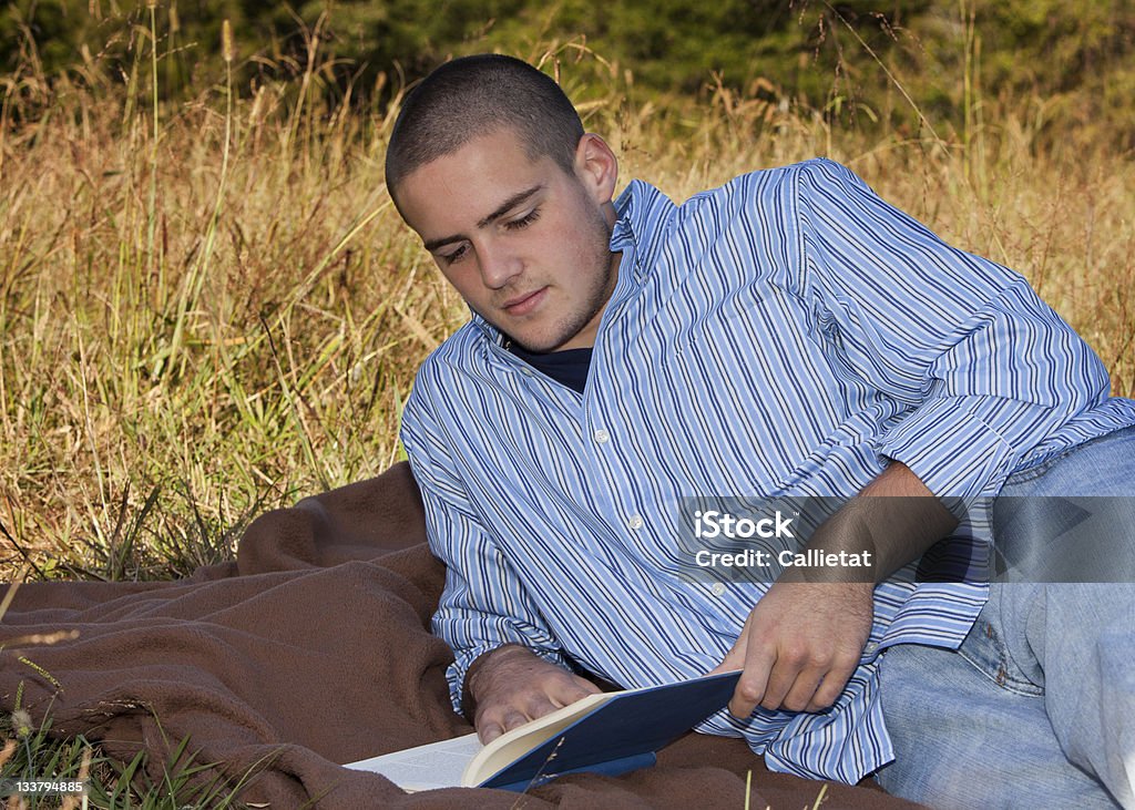 Mentir jeune garçon lisant un livre à l'extérieur - Photo de Hommes libre de droits
