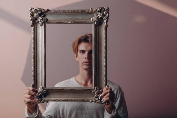 istock Portrait young man standing with picture frame at studio. 1337955849