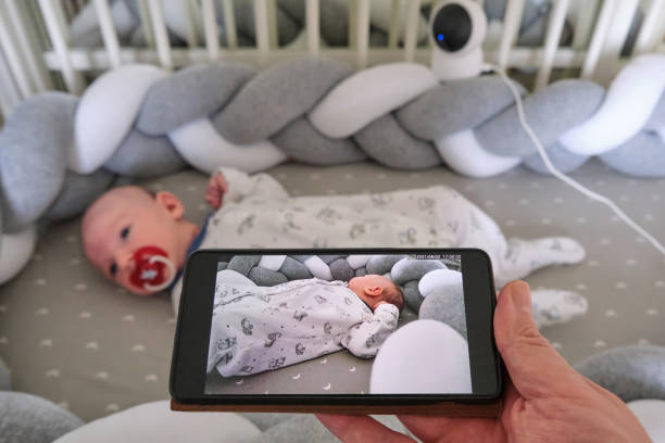 überwachung eines neugeborenen in einem kinderbett durch eine heimüberwachungskamera online und das internet in einem mobiltelefon - phone cradle stock-fotos und bilder